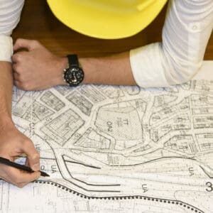 A person with a yellow hard hat is drawing on a map.