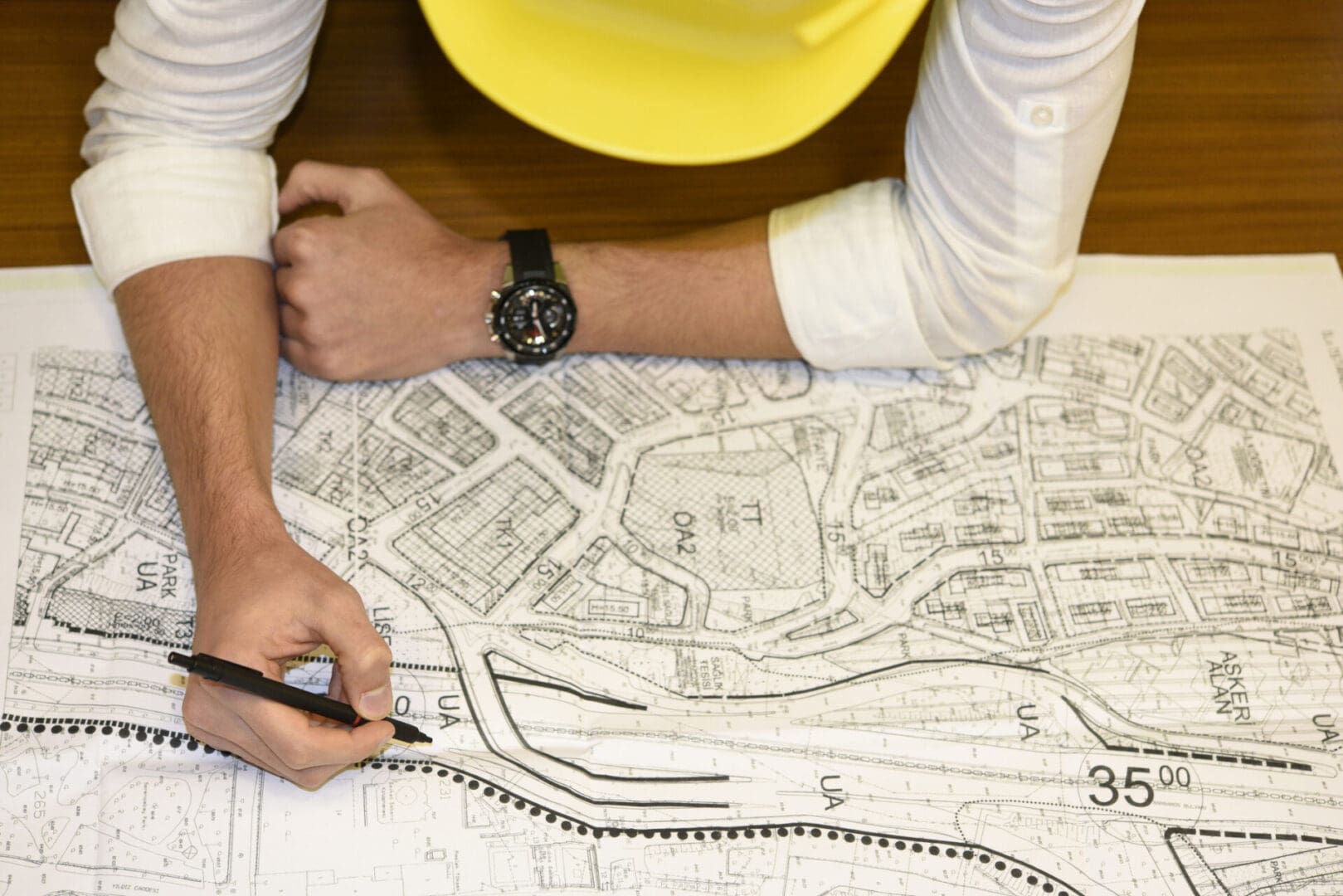 A person with a yellow hard hat is drawing on a map.