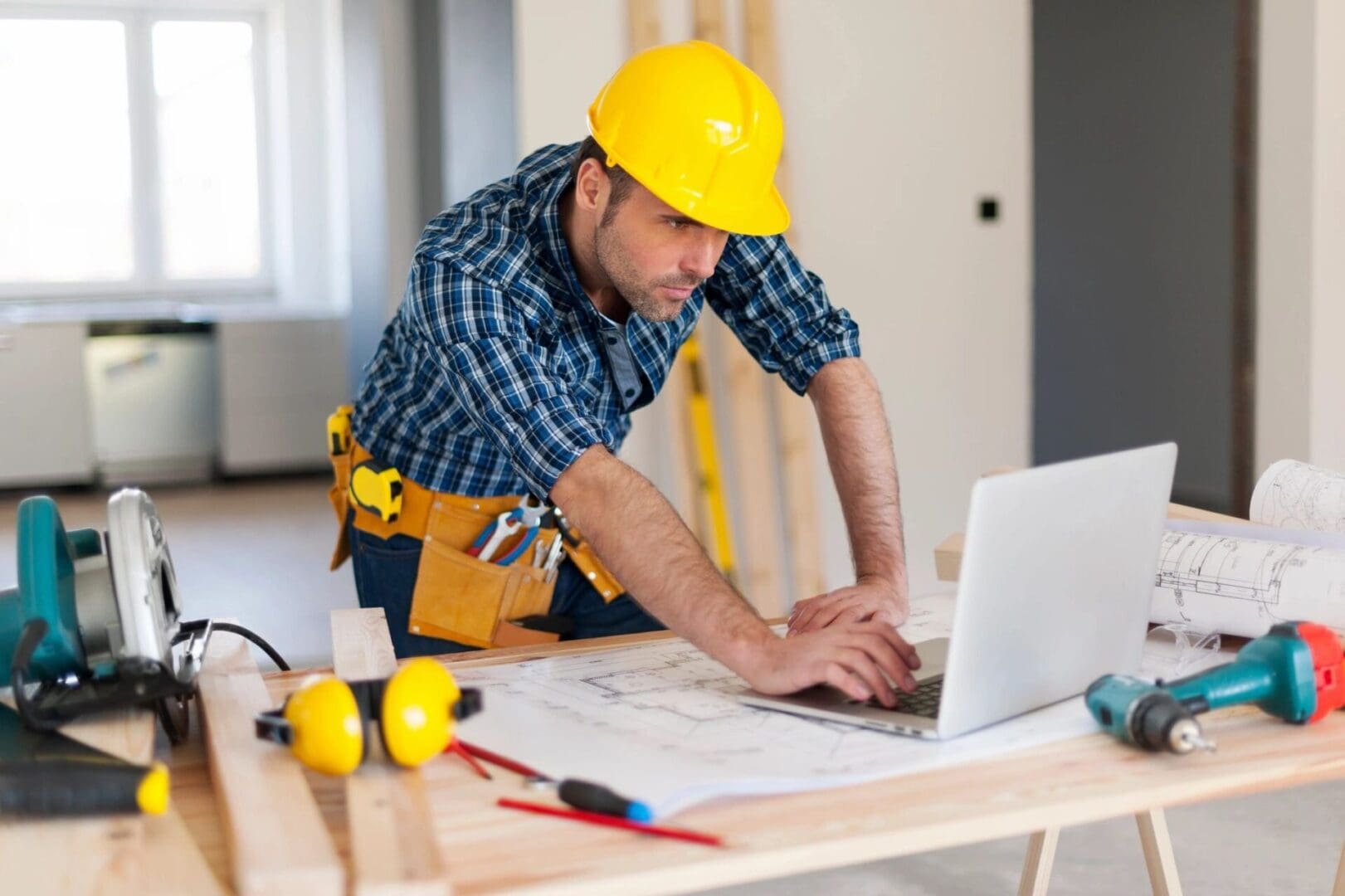 A man in yellow hard hat using laptop on table.